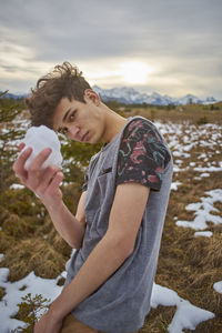 Portrait of young man holding snow while standing on field