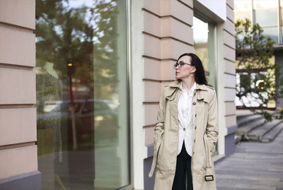 Woman looking away while standing against glass wall
