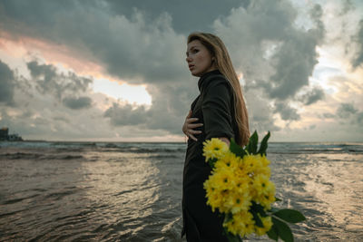 Portrait of young woman standing by lake against sky during sunset