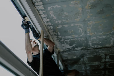 One young worker is repairing a window frame from the outside. person