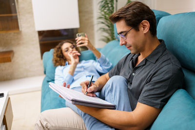 Friends using mobile phone while sitting on sofa at home