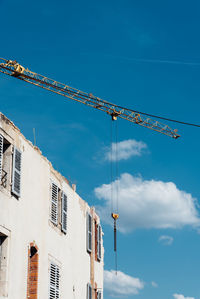 Low angle view of crane by building against sky