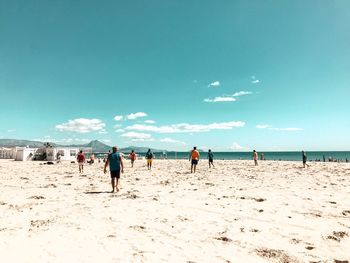 Group of people at beach against sky during sunny day