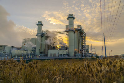 Low angle view of industry on field against sky during sunset