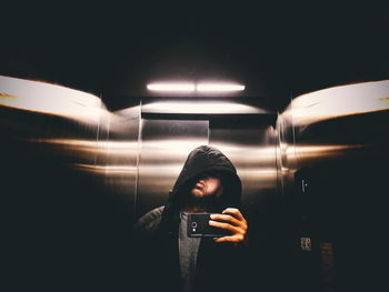 Young man taking selfie with smart phone while standing in elevator