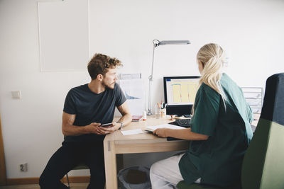 Male patient looking while female nurse using computer at office in hospital