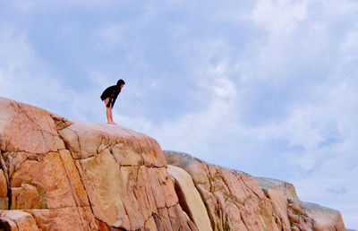 Low angle view of woman standing on rock formation against sky