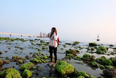 Full length of woman photographing at beach against sky