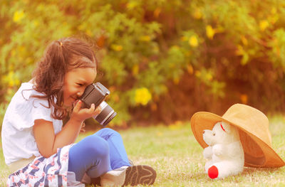 Woman photographing with toy while sitting on field