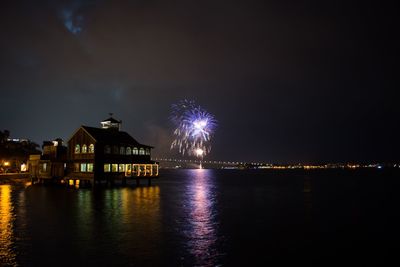 Firework display over river by illuminated buildings in city at night
