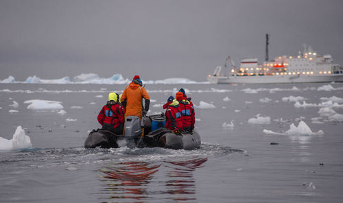 Rear view of people on inflatable raft amidst icebergs in sea during winter