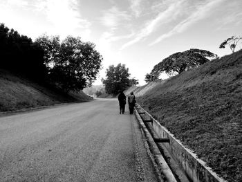 Rear view of people walking on road amidst trees