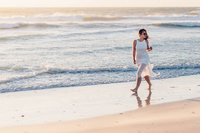 Young woman walking at shore against clear sky during sunset