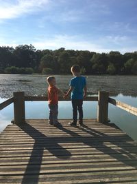 Rear view of boy standing on lake against sky