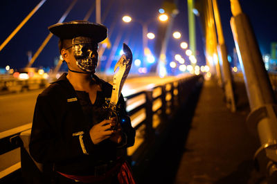 Man wearing mask holding knife on bridge at night