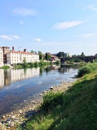 Buildings by river against blue sky