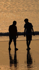 Silhouette men standing on beach against sky during sunset