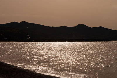 Calm sea in front of mountains against clear sky
