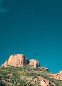 Bird flying over rock against blue sky