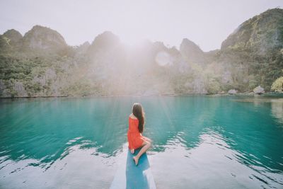 Side view of woman relaxing on jetty on sea by mountains against sky at coron island