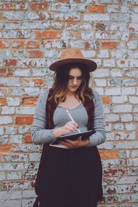Portrait of young woman standing against brick wall
