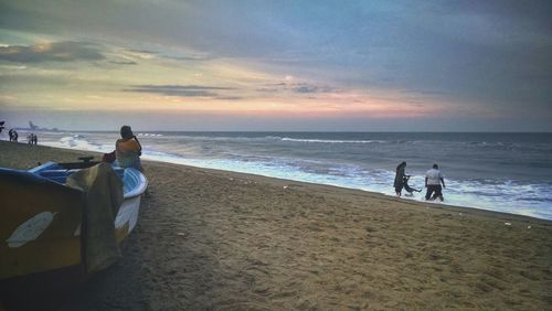 People standing on beach against sky during sunset