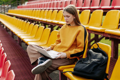 A young girl is doing her homework using a laptop in the stands of the stadium. 