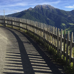 Shadow of fence on road against mountain range