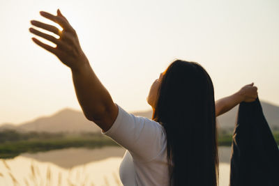 Rear view of woman with arms raised against sky during sunset