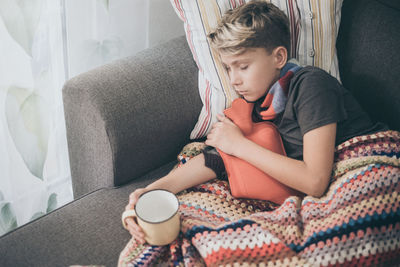 Ill boy sleeping with hot water bottle on sofa