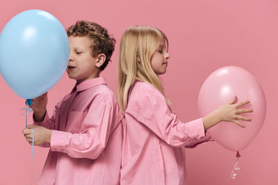 Smiling boy and girl with balloons standing against pink background