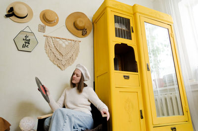 Young woman in beret sits in cozy home, room with music record in hands. vintage yellow cabinet.