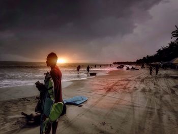 People at beach against sky during sunset