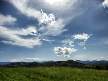 Scenic view of grassy landscape against cloudy sky on sunny day