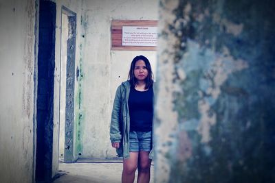 Portrait of young woman standing against wall