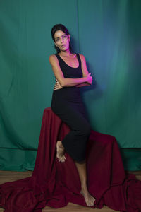 Portrait of adult model sitting on wooden chair against dark green background. 