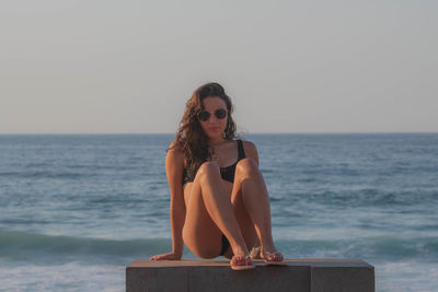 Full length of teenage girl wearing sunglasses sitting on pier against sea