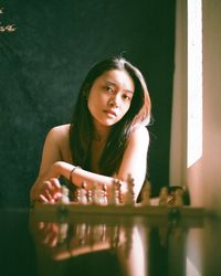 Portrait of young woman sitting by chess pieces on table