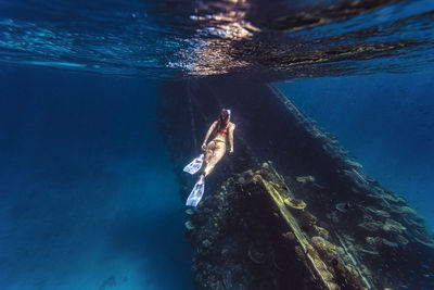 Woman wearing diving flippers swimming over shipwreck in sea