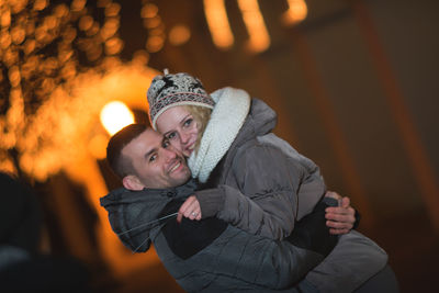 Smiling young man carrying woman at night during winter