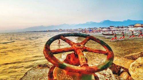 Rusty wheel on beach against sky