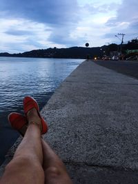 Low section of person relaxing by sea against sky