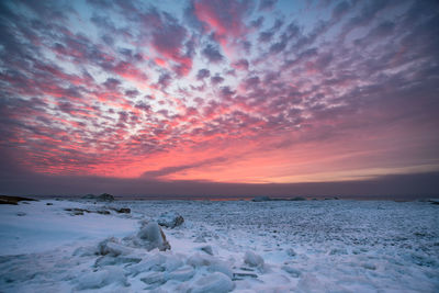 Frozen sea against cloudy sky during sunset