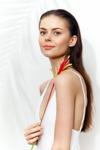 Portrait of smiling young woman with arms crossed standing against white background