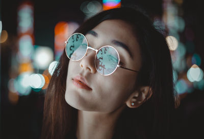 Close-up of woman wearing eyeglasses standing outdoors at night