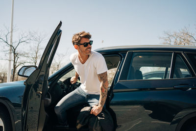 Man with umbrella on car against sky