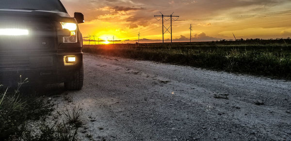 Road amidst field against sky at sunset