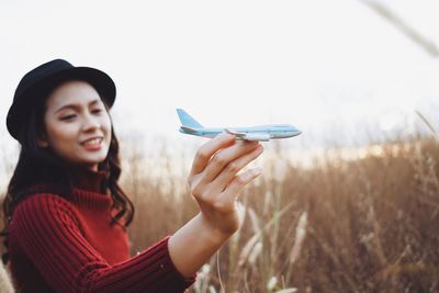 Smiling young woman holding hat on field