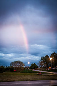 Rainbow over illuminated city against sky at dusk