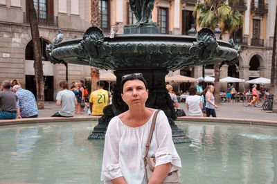 Woman sitting against fountain in city
